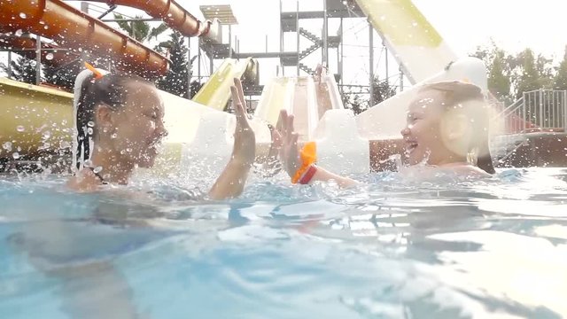 little girl is playing with her mother in water park, swimming in a pool, clapping their hands and laughing
