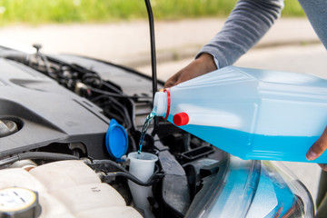 Junge Frau f&uuml;llt bei ihrem PKW Scheibenreiniger nach