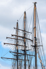 masts and rigging of a historic three-master sailing ship against the cloudy sky, travel and voyage concept, vertical