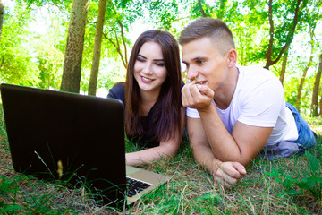 .guy with a girl lie on the grass in front of a laptop