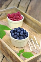 Healthy food,agriculture,harvest and fruit concept: fresh ripe blueberries and raspberries in two bowls on a wooden tray.