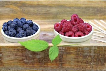 Healthy food,agriculture,harvest and fruit concept: fresh ripe blueberries and raspberries in two bowls on a wooden tray.