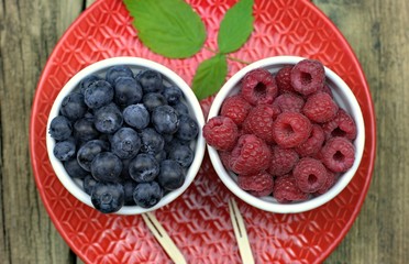 Healthy food,agriculture,harvest and fruit concept: ripe blueberries and raspberries in two bowls on a red ceramic plate.