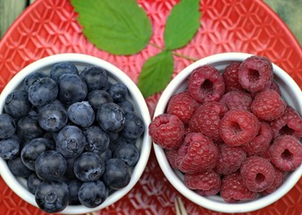 Healthy food,agriculture,harvest and fruit concept: ripe blueberries and raspberries in two bowls on a red ceramic plate.