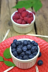 Healthy food,agriculture,harvest and fruit concept: ripe blueberries and raspberries in two bowls on a red ceramic plate.