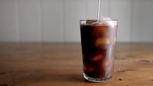 Slow motion of cream being poured into a glass of cold brew iced coffee.