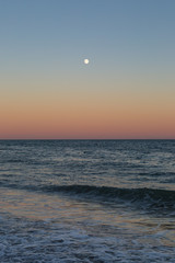 A full moon visible at sunset, over the sea at Brighton