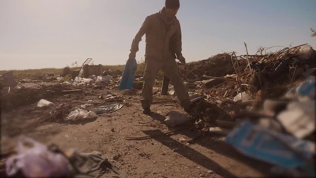 dirty male homeless hungry man in a dump looking for clothing food in the package with walking goes looking for food slow motion video. homeless dirty lifestyle man roofless person looking for food in