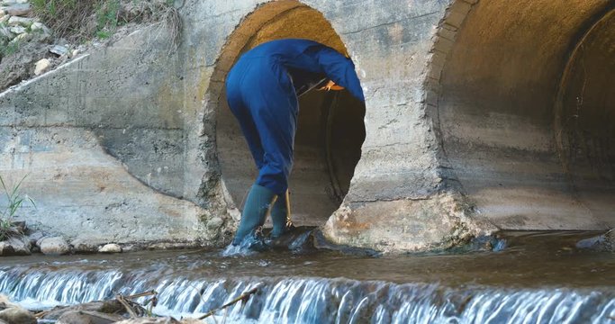 Engineer, worker checks gutters, in blue robe, in boots, in a construction yellow helmet, tunnels, technical supervision.