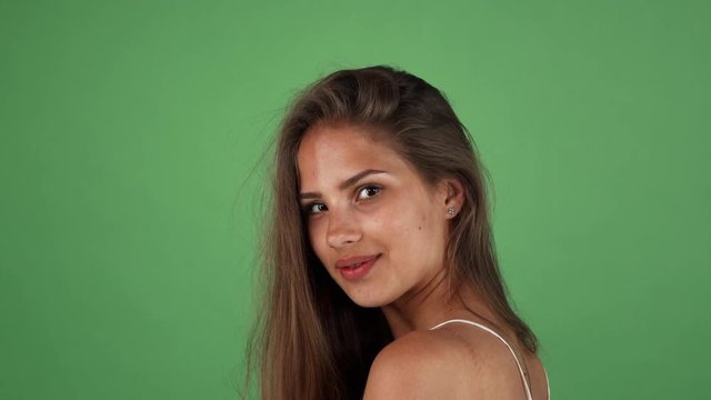 Gorgeous sexy young long haired cheerful woman with smooth perfect tanned skin smiling to the camera over her shoulder, posing on green background at studio, copy space.