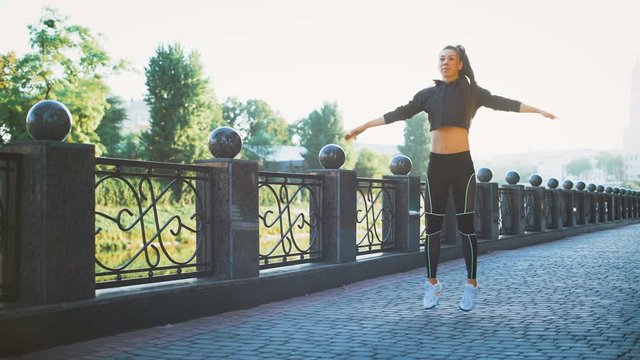Active woman exercising and jumping in city park. Attractive fit girl training warming up at morning outdoors. Healthy, fitness, wellness lifestyle. Sport, cardio, workout concept
