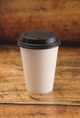 Disposable White Paper Coffee Cup with a Black Lid on a Wooden Counter