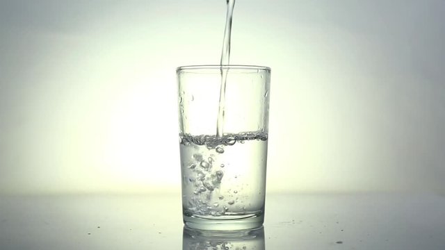 video footage spilled pure water into transparent glass, white gradual background