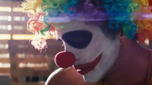 Close up sad crazy clown smoking a cigarette with anamorphic lens flare