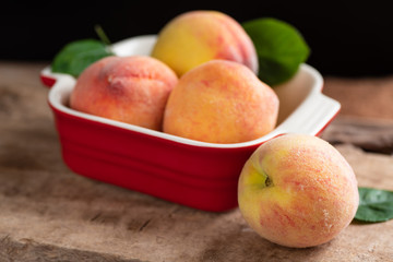 Ripe peaches in a red bowl on wooden, tropical fruit