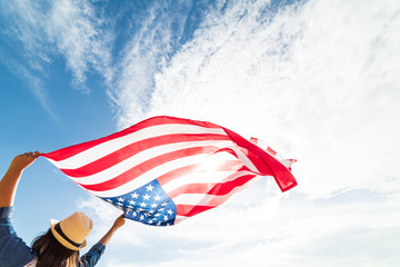 Close up young happy woman holding United States of America flag and running, jumping carefree with open arms with blue sky. USA Independence day, 4 July.