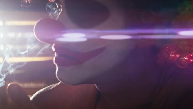 Close up of clown with heavy make-up smoking anamorphic light flare