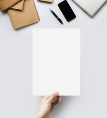 Hands holding blank paper sheet A4 size at table work space top view.