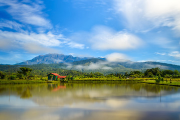Serene morning view of the Mount Kinabalu and rainforest hills. Beautiful reflection on a recreational fishing pond in Ranau, Sabah, Malaysia.