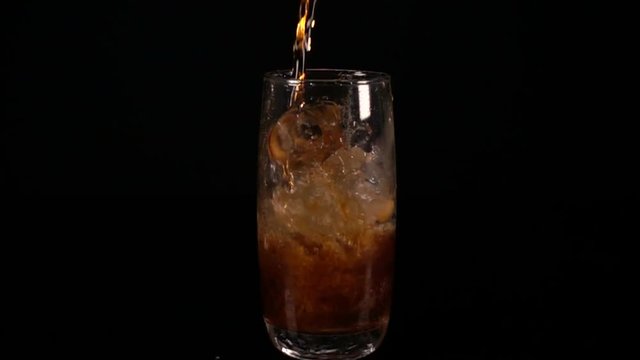 Pour Cola into a glass with ice. Slow motion. 
