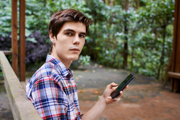 Fototapeta premium Man is sitting in the wooden pavilion and looking at the cellphone in the forest