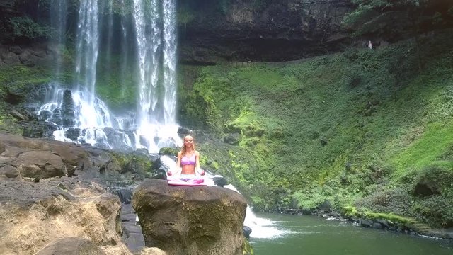 lady meditates in lotus pose against foamy waterfall