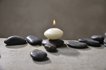 Fototapeta na wymiar Candle with pile of black stones on gray background 