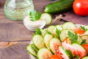 Vegetable salad of fresh cucumbers, tomatoes, parsley and sesame seeds on a plate on a wooden table