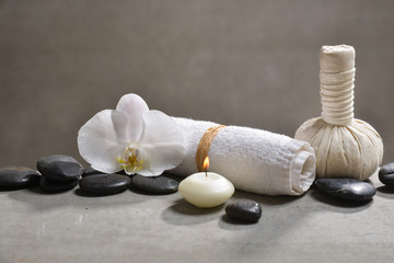 candle with pile of black stones and white orchid, herbal ball.towel on gray background