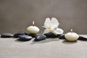 Fototapeta na wymiar candle with pile of black stones and white orchid, on gray background