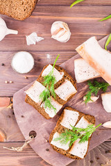 Sandwiches from rye bread, salted bacon and dill on a cutting board on a wooden table. Top view
