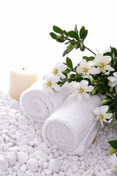 Rolled towel and candle and gardenia on white pebbles 
