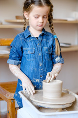 Fototapeta na wymiar pottery handcraft hobby. little girl forming and shaping clay jug on potter wheel
