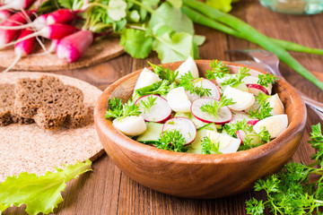 Delicious spring vegetable salad from cucumber, radish, quail eggs, greens and oil in a plate on a wooden table