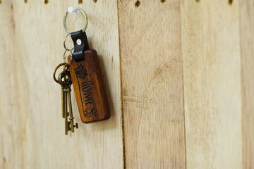 House key with wooden home keyring hanging on wood board background, property concept, copy space