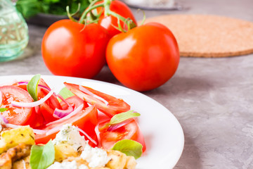 Fried zucchini with feta cheese, tomatoes, herbs and onions on a plate on a table
