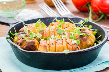 Baked young potatoes in spices and oil with arugula in a iron pan on a wooden table
