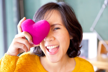 Young cute asian woman with pink heart-shaped pillow