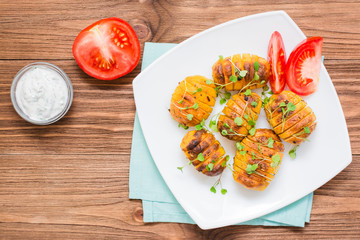 Baked young potatoes in spices and oil with arugula on a plate  and sour cream on a wooden table. Top view. Copy space