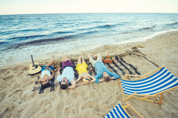 multiracial young people lying on blanket while spending time on sandy beach