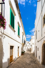 A beautiful narrow street in  Locorotondo, with typical whitewashed houses and colorful green shutters, Apulia, Italy