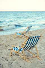 selective focus of wooden beach chairs on sandy beach with sea on background
