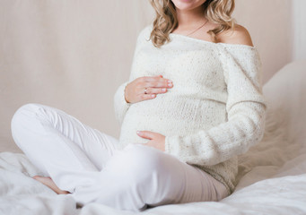 A beautiful pregnant woman sits with legs crossed and gently hugs her tummy