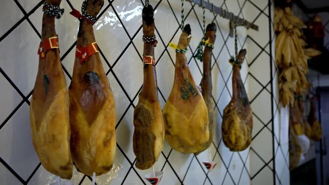 4K, Dried pork thighs hang on the meat market. Spanish national dish of ham or jamon in a grocery. Iberian pork shopping in supermarket Spain. Dry-Cured Ham hanging. Market sell raw meat products-Dan