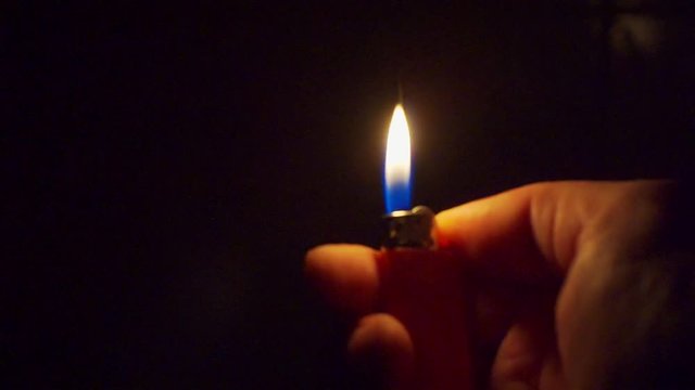 hand holds a burning lighter in the dark