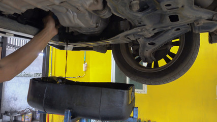 Mechanic draining engine oil from a car for an oil change.