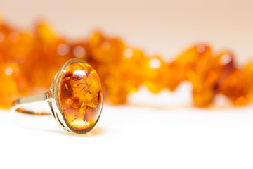 Bernsteinkette und Bernsteinring vor weißem Hintergrund, In Gold gefasster Bernstein als Ring