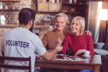 You can do it. Back view of bearded volunteer that stretching right arm and giving puzzle to his friend