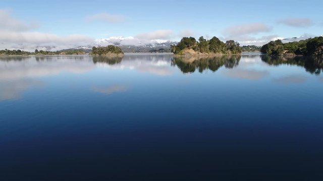 Aerial drone scene of Alumine lake, in Villa Pehuenia, Moquehue, Neuquen, Patagonia Argentina. Camera passing over an islands discovering landscape. Mountains with snow and low clouds.