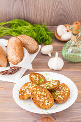 Fresh rye garlic croutons with dill on a plate and buns in a basket on a wooden table